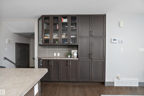 The property features built-in cabinetry with glass-fronted upper cabinets, a light-colored countertop, and a tiled backsplash - 7776 Eifert Crescent Nw, Edmonton, AB - Indoor