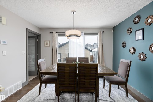 Dining area featuring a modern chandelier, hardwood flooring, and a large window providing natural light - 7776 Eifert Crescent Nw, Edmonton, AB - Indoor Photo Showing Dining Room
