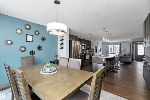 The property features an open-concept living space with dark wood flooring, a dining area with a modern chandelier, and a kitchen with stainless steel appliances and dark cabinetry - 7776 Eifert Crescent Nw, Edmonton, AB - Indoor Photo Showing Dining Room
