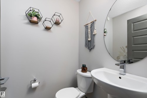 The bathroom features a white pedestal sink with a chrome faucet, a round wall-mounted mirror, and light gray walls - 7776 Eifert Crescent Nw, Edmonton, AB - Indoor Photo Showing Bathroom