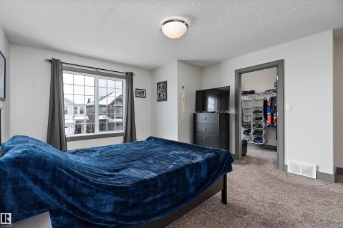 This room features a window with white framing and dark grey curtains, a flush-mount ceiling light, and neutral-toned carpeting - 7776 Eifert Crescent Nw, Edmonton, AB - Indoor Photo Showing Bedroom