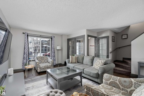 Well-appointed living area featuring hardwood flooring, a large window with white grilles, and a staircase with a dark handrail - 7776 Eifert Crescent Nw, Edmonton, AB - Indoor Photo Showing Living Room