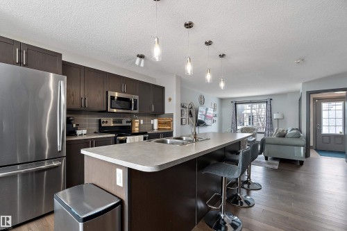 The kitchen features stainless steel appliances, dark wood cabinetry, and a central island with a sink and seating - 7776 Eifert Crescent Nw, Edmonton, AB - Indoor Photo Showing Kitchen With Double Sink With Upgraded Kitchen