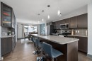The kitchen features dark wood cabinetry, stainless steel appliances, a large island with a light-colored countertop, and pendant lighting - 7776 Eifert Crescent Nw, Edmonton, AB  - Indoor Photo Showing Kitchen With Upgraded Kitchen 