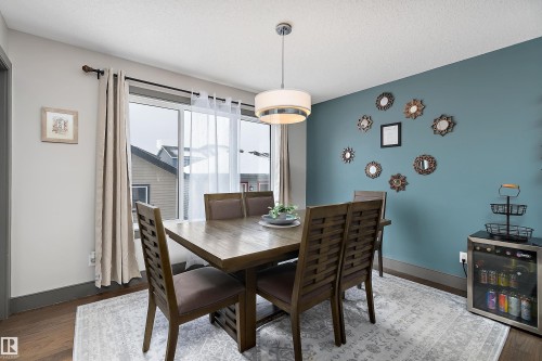 The dining area features a large window with sheer and blackout curtains, a contemporary light fixture, and a decorative accent wall - 7776 Eifert Crescent Nw, Edmonton, AB - Indoor Photo Showing Dining Room