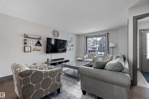 The living area features a large window with white casing, a ceiling with a textured finish, and light-colored walls - 7776 Eifert Crescent Nw, Edmonton, AB - Indoor Photo Showing Living Room