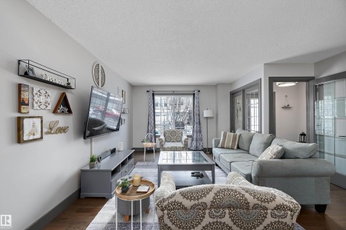 Living area featuring hardwood flooring, a large window with patterned curtains, and light gray walls - 7776 Eifert Crescent Nw, Edmonton, AB - Indoor Photo Showing Living Room