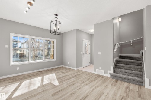 Inviting interior space featuring light-colored flooring, a prominent window, and a carpeted staircase with a handrail - 4016 Allan Crescent, Edmonton, AB - Indoor Photo Showing Other Room