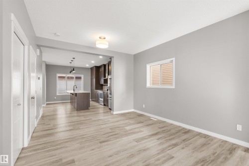 Open concept living area featuring light-toned flooring, neutral gray walls, and a window with horizontal blinds - 4016 Allan Crescent, Edmonton, AB - Indoor Photo Showing Other Room