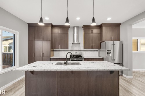 The kitchen features an island with a sink and a black faucet, granite countertops, dark wood cabinetry, and stainless steel appliances - 4016 Allan Crescent, Edmonton, AB - Indoor Photo Showing Kitchen With Upgraded Kitchen