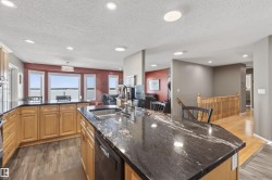The kitchen features light wood cabinetry, dark granite countertops, and a stainless steel sink with a gooseneck faucet - 