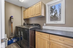 This utility room features light wood cabinetry, a dark countertop, and a window providing natural light and a view of trees - 