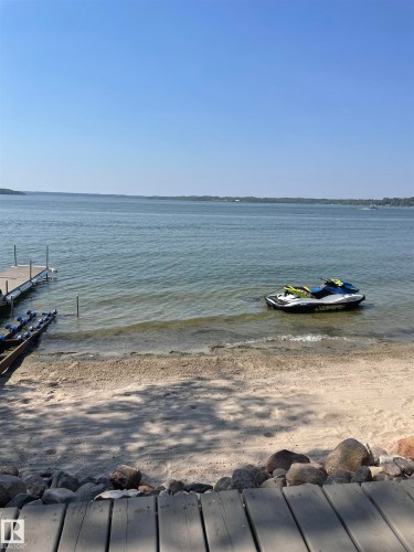 The property features a sandy beach area with clear water, a private dock, and a wide lake view - #12 61212  Rr 463, Rural Bonnyville M.D., AB - Outdoor With Body Of Water With View