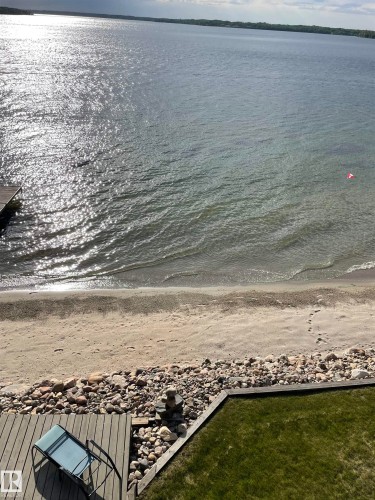 This property offers a serene waterside setting with a sandy beach and a wooden deck, complemented by a patch of green lawn - #12 61212  Rr 463, Rural Bonnyville M.D., AB - Outdoor With Body Of Water With View