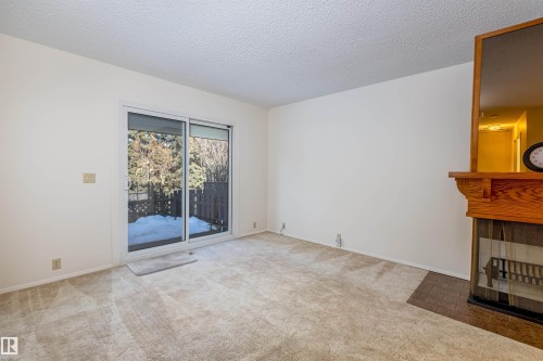 The room features a sliding glass door, a fireplace with a wood mantel, and carpeted floors - 108 Forest Grove, St. Albert, AB - Indoor Photo Showing Other Room