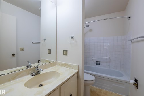 The bathroom features a vanity with a light-colored countertop and an integrated sink, a large wall-mounted mirror, and a bathtub with white tiled walls - 108 Forest Grove, St. Albert, AB - Indoor Photo Showing Bathroom