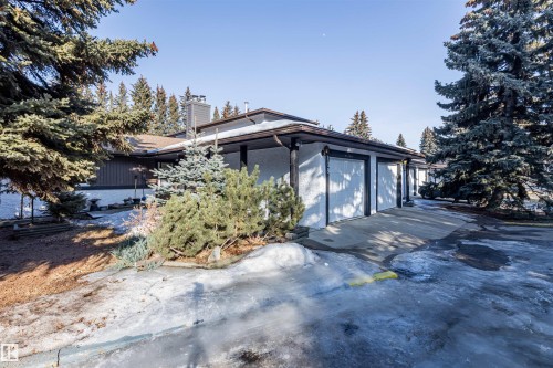 The property features a brown roof, white garage doors, and a well-maintained exterior with mature evergreen trees and shrubs - 108 Forest Grove, St. Albert, AB - Outdoor