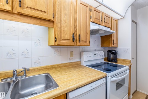 The kitchen features wood cabinetry, a double basin stainless steel sink, a white electric range, and a white dishwasher - 108 Forest Grove, St. Albert, AB - Indoor Photo Showing Kitchen With Double Sink