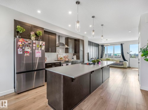The open concept main living area features a kitchen with dark cabinetry, stainless steel appliances, and a large island with a light-colored countertop - 2636 192 Street, Edmonton, AB - Indoor Photo Showing Kitchen With Upgraded Kitchen