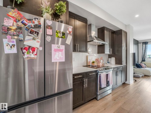This kitchen features dark wood cabinetry, a stainless steel refrigerator, and a stainless steel oven with an overhead range hood - 2636 192 Street, Edmonton, AB - Indoor Photo Showing Kitchen With Upgraded Kitchen