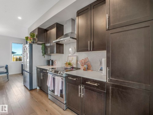 Kitchen featuring dark wood cabinetry, stainless steel appliances, light countertops, and a white tiled backsplash - 2636 192 Street, Edmonton, AB - Indoor Photo Showing Kitchen With Upgraded Kitchen