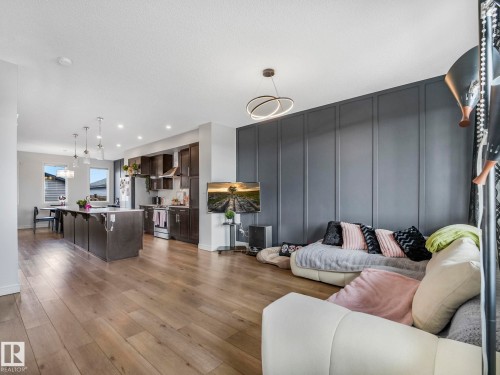 Open concept living area featuring light wood flooring, a kitchen with dark cabinetry and an island, and a living area with a dark paneled accent wall - 2636 192 Street, Edmonton, AB - Indoor Photo Showing Living Room