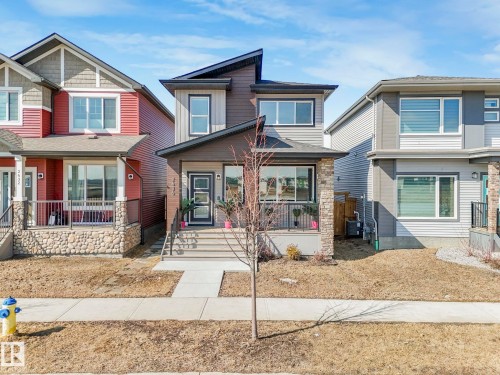 The property presents a modern facade with varying shades of gray and brown siding, a dark gray front door, and a covered porch supported by a stone-clad pillar - 2636 192 Street, Edmonton, AB - Outdoor With Facade