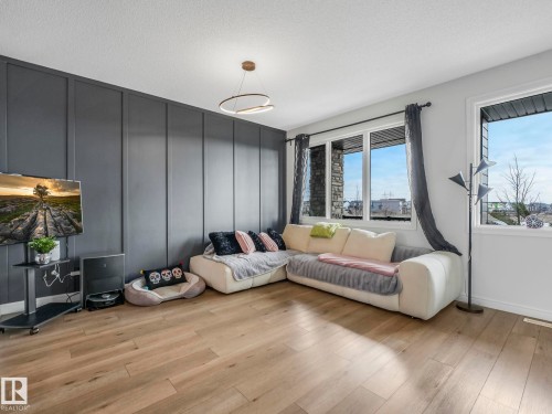 Living area featuring light wood flooring, a dark accent wall with vertical paneling, and large windows that provide natural light - 2636 192 Street, Edmonton, AB - Indoor Photo Showing Living Room