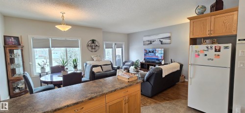 The open concept living area features a dining space with a window overlooking the outdoors, and a living area with light-colored walls and a television - 5514 49 Street, Vegreville, AB - Indoor