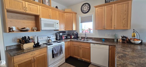 The kitchen features wooden cabinetry, a white microwave, a white range, and a white dishwasher - 5514 49 Street, Vegreville, AB - Indoor Photo Showing Kitchen With Double Sink