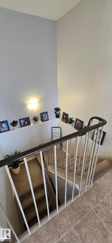 Staircase with carpeted steps and a white and black railing, featuring a wall sconce and light-colored walls - 5514 49 Street, Vegreville, AB - Indoor