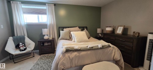 Bedroom featuring a window with white curtains, a bed with a dark metal frame, and a dark wood dresser - 5514 49 Street, Vegreville, AB - Indoor Photo Showing Bedroom
