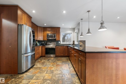 The kitchen features wood cabinetry, stainless steel appliances, a dark countertop, and stone tile flooring - 101 Westridge Road, Edmonton, AB - Indoor Photo Showing Kitchen