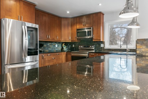 Modern kitchen featuring stainless steel appliances, wood cabinetry, a tiled backsplash, and a spacious island with a dark countertop - 101 Westridge Road, Edmonton, AB - Indoor Photo Showing Kitchen