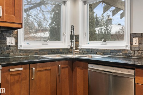 The kitchen features a corner double-basin stainless steel sink with a high-arc faucet, set against a dark countertop and a natural stone-look tile backsplash - 101 Westridge Road, Edmonton, AB - Indoor Photo Showing Kitchen With Double Sink