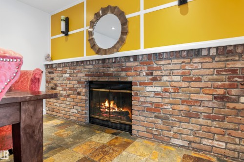 This inviting space features a brick fireplace with a visible fire, set against a rich yellow wall with decorative white trim - 101 Westridge Road, Edmonton, AB - Indoor With Fireplace