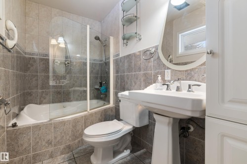 Bathroom featuring a pedestal sink, a toilet, and a bathtub with a glass shower screen, all surrounded by tiled walls - 101 Westridge Road, Edmonton, AB - Indoor Photo Showing Bathroom