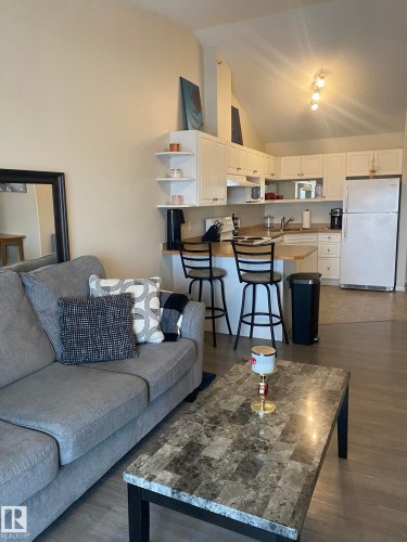 Open concept living area featuring a kitchen with white cabinetry and a breakfast bar, and a living area with light-colored walls and wood-look flooring - 336 9525 162 Avenue, Edmonton, AB - Indoor