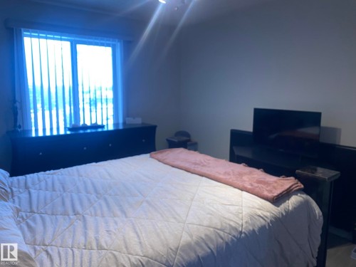 The bedroom features a large window with vertical blinds, providing natural light, and a dark dresser below it - 336 9525 162 Avenue, Edmonton, AB - Indoor Photo Showing Bedroom
