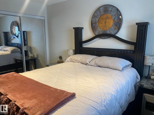 Bedroom featuring a dark wood bed frame with an ornate headboard, light-colored walls, and a large wall clock - 336 9525 162 Avenue, Edmonton, AB - Indoor Photo Showing Bedroom