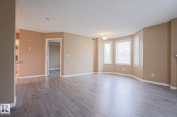 Spacious living area featuring light-toned flooring, a bay window with blinds, and neutral wall colors - 