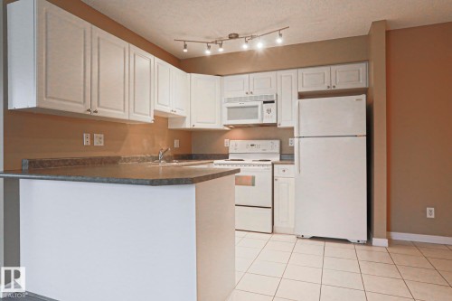 The kitchen features white cabinetry, a white refrigerator, and a white oven with a matching microwave - 201 10909 103 Avenue Nw, Edmonton, AB - Indoor Photo Showing Kitchen With Double Sink