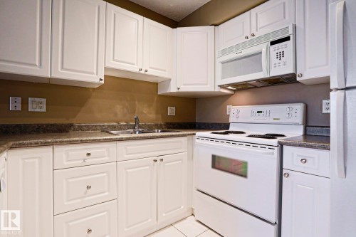 The kitchen features white cabinetry, a stainless steel sink, a white oven/range, and a white microwave - 201 10909 103 Avenue Nw, Edmonton, AB - Indoor Photo Showing Kitchen With Double Sink