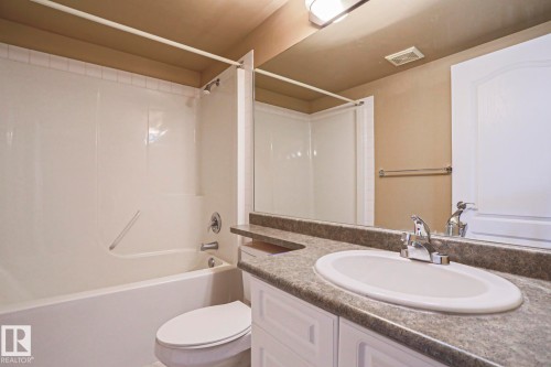 Bathroom featuring a white bathtub with a shower, a toilet, and a vanity with an integrated sink and chrome faucet - 201 10909 103 Avenue Nw, Edmonton, AB - Indoor Photo Showing Bathroom