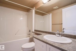 Bathroom featuring a white bathtub with a shower, a toilet, and a vanity with an integrated sink and chrome faucet - 