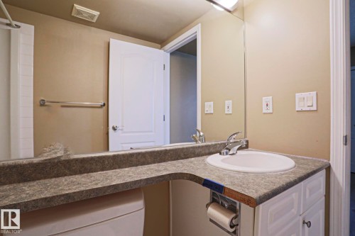 Bathroom featuring a vanity with a white basin and chrome faucet, a large mirror, and a toilet - 201 10909 103 Avenue Nw, Edmonton, AB - Indoor Photo Showing Bathroom