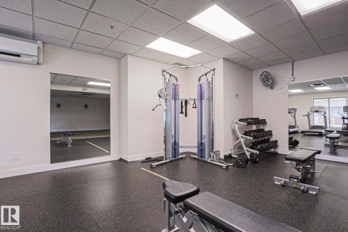 This property features a fitness area with specialized flooring, mirrored walls, and various exercise equipment including a weight rack, cable machine, and exercise benches - 201 10909 103 Avenue Nw, Edmonton, AB - Indoor Photo Showing Gym Room