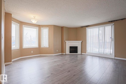 Spacious living area featuring light-toned flooring, a fireplace with a white mantel, and ample natural light from multiple windows and a glass sliding door - 201 10909 103 Avenue Nw, Edmonton, AB - Indoor Photo Showing Living Room With Fireplace