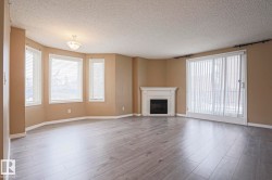 Spacious living area featuring light-toned flooring, a fireplace with a white mantel, and ample natural light from multiple windows and a glass sliding door - 