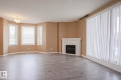 Spacious living area featuring light-colored flooring, a decorative corner fireplace with a white mantel, and a bay window with three window panes - 